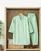 Light green shirt and pants hanging in a wooden wardrobe with a plant and basket in the background.