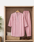 Pink shirt and pants hanging on a wooden rack with a plant and basket in the background.